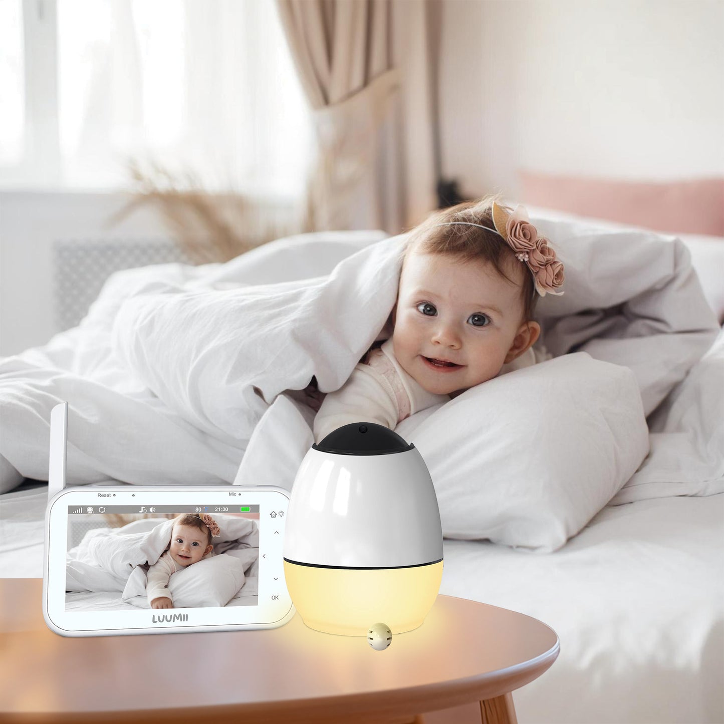 Baby som smiler i sengen mens Luumii babymonitor med nattlys står på nattbordet i forgrunnen
