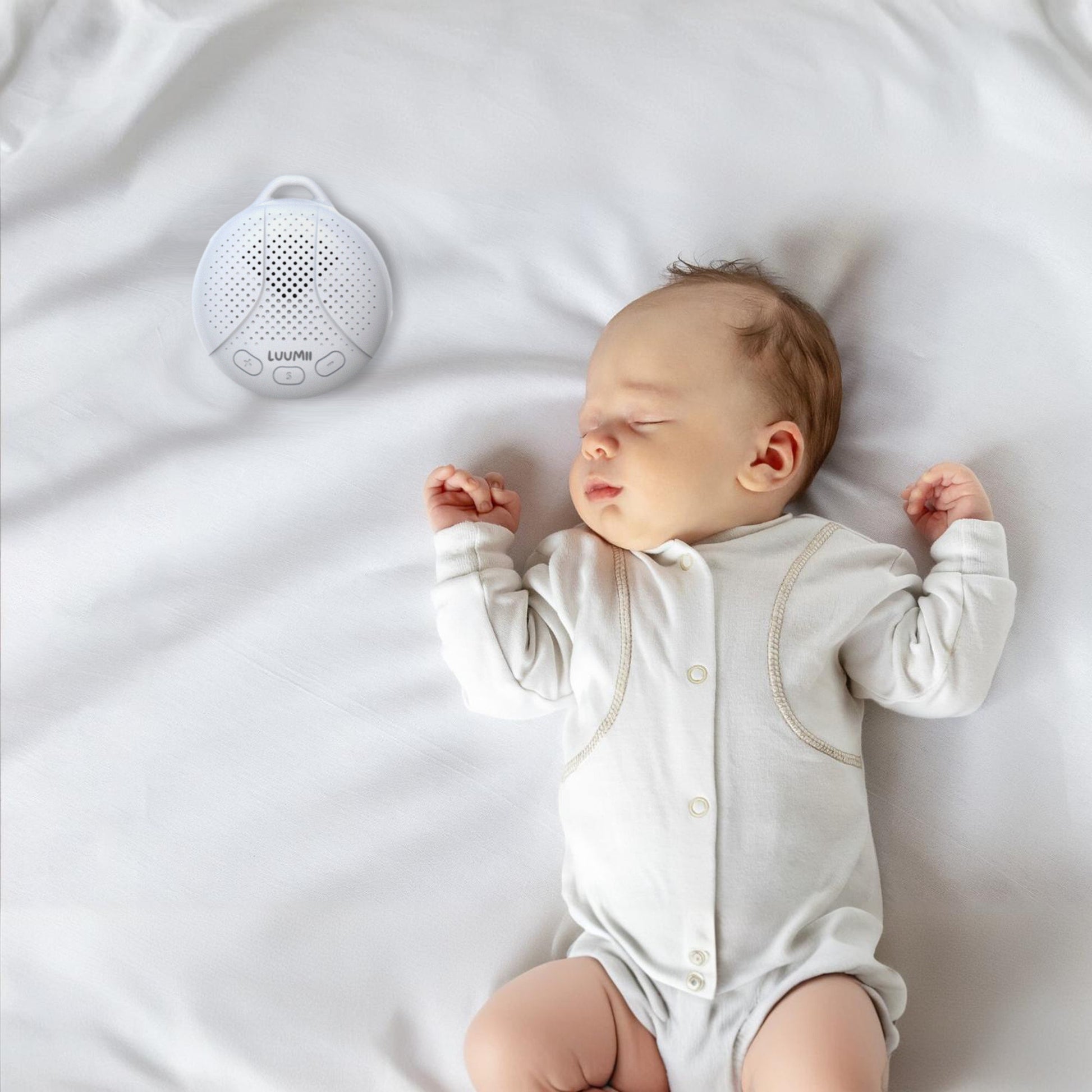 Baby som sover trygt i sengen med Luumii bærbar white noise-maskin ved siden av.