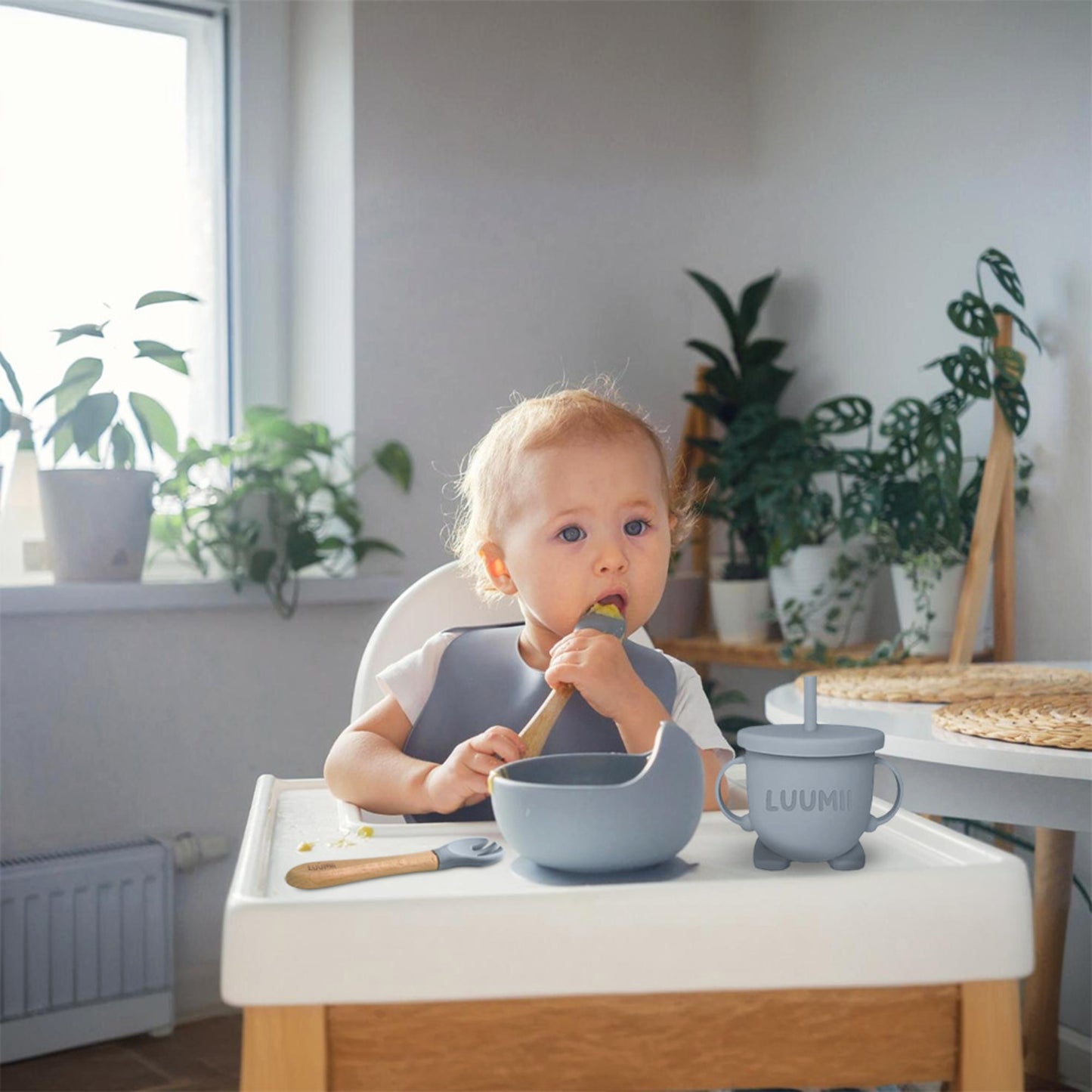 Baby som spiser med Luumii barneservice i blå farge, inkludert bolle, kopp og bestikk på høystol