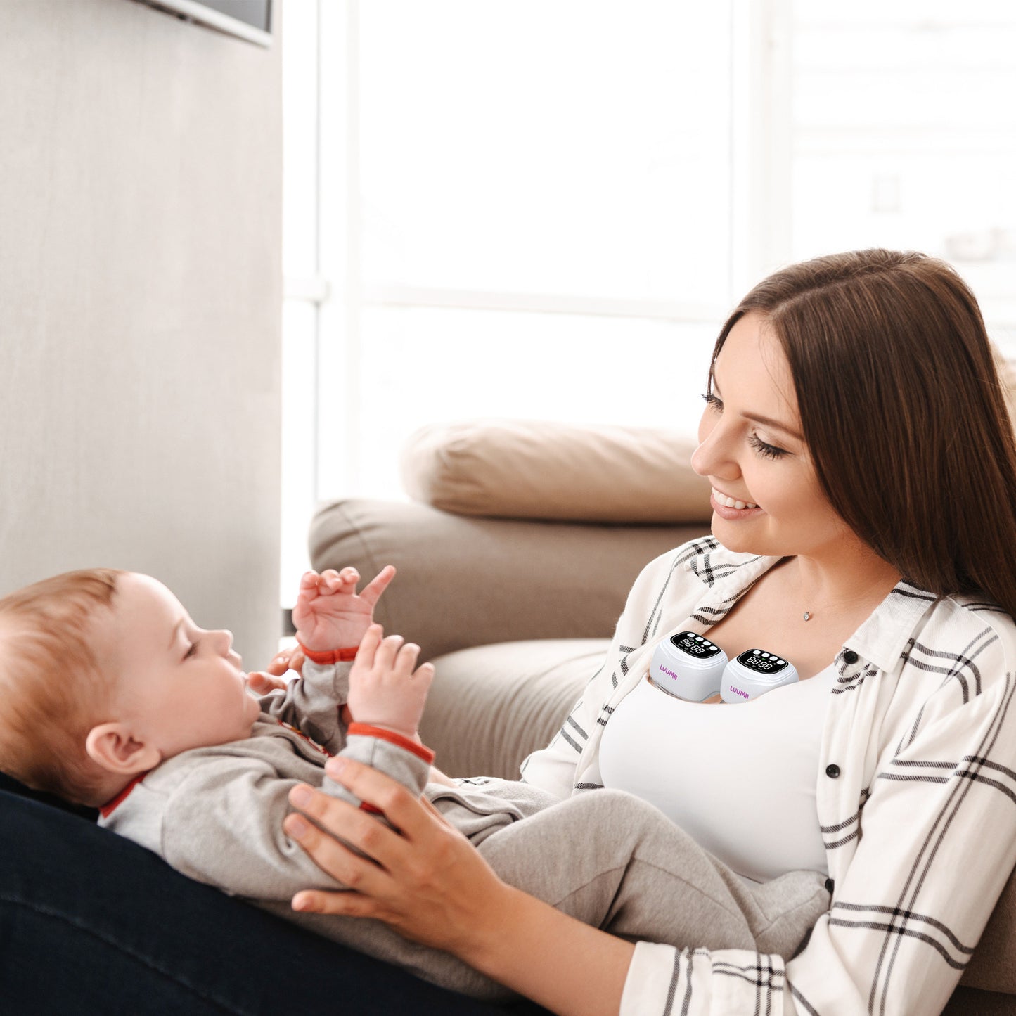 Mor som bruker Luumii bærbar brystpumpe mens hun holder babyen i armene hjemme.